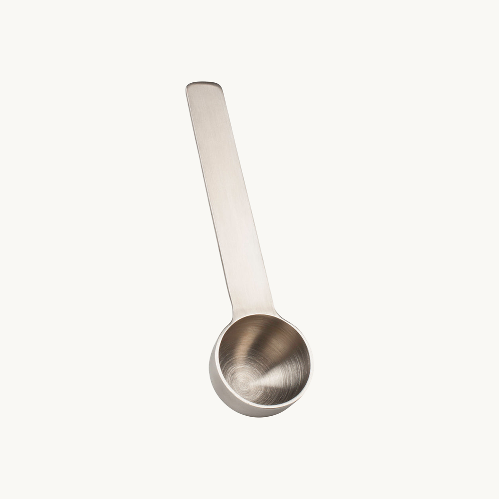 Silver coffee scoop overflowing with ground coffee